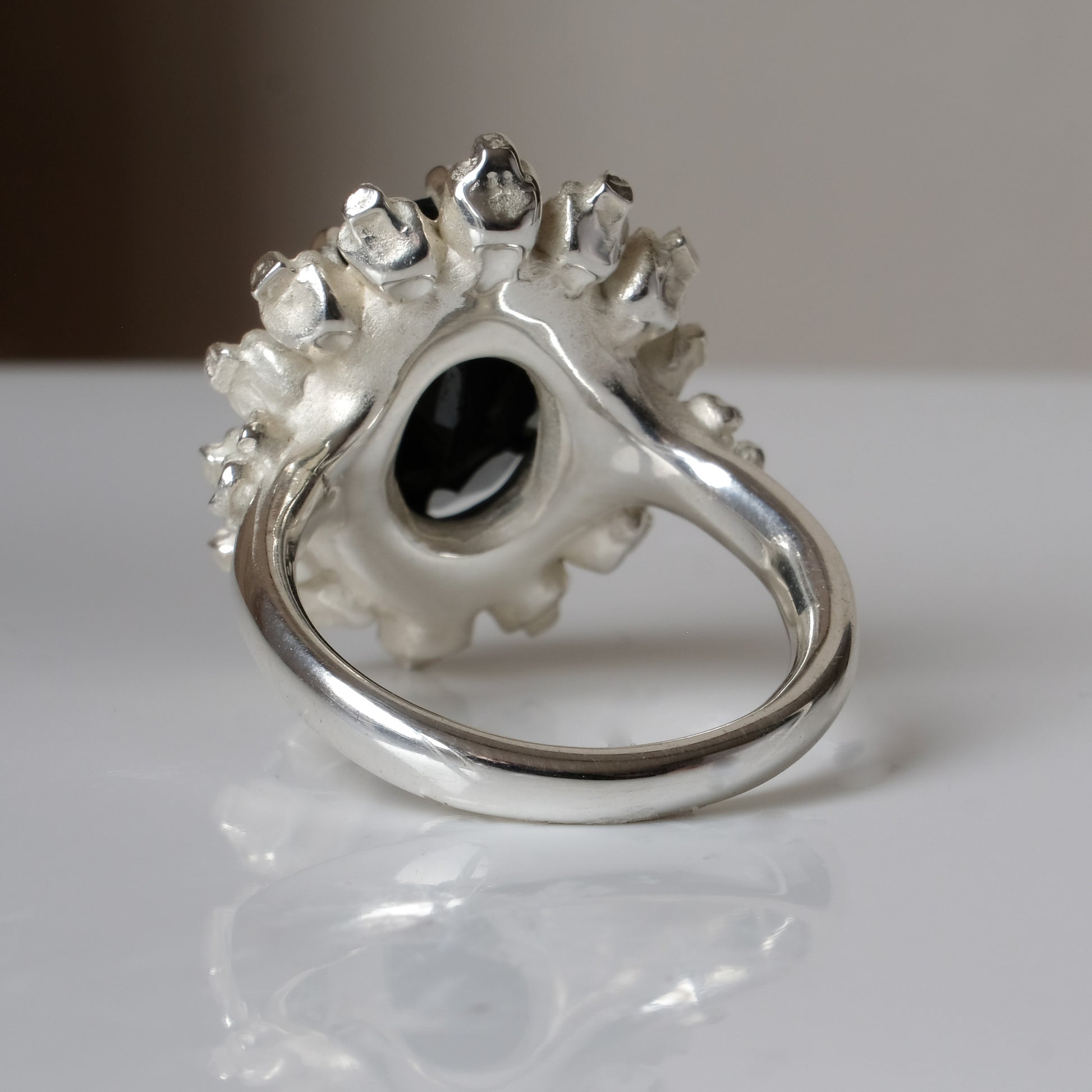Ring with claw set black spinel gemstone and silver skull design on a white background