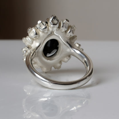 Ring with claw set black spinel gemstone and silver skull design on a white background