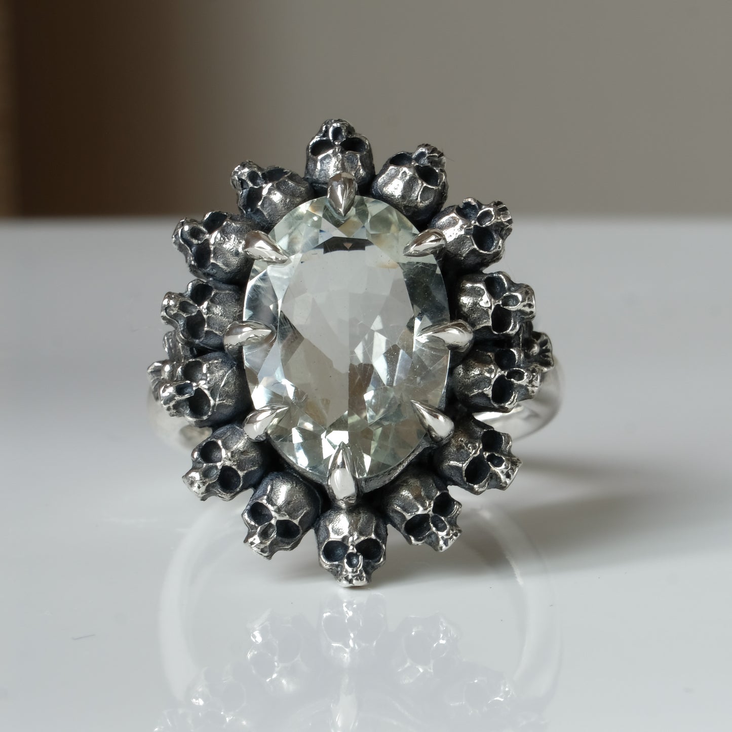 Ring with claw set with mint quartz gemstone and silver skull design on a white background