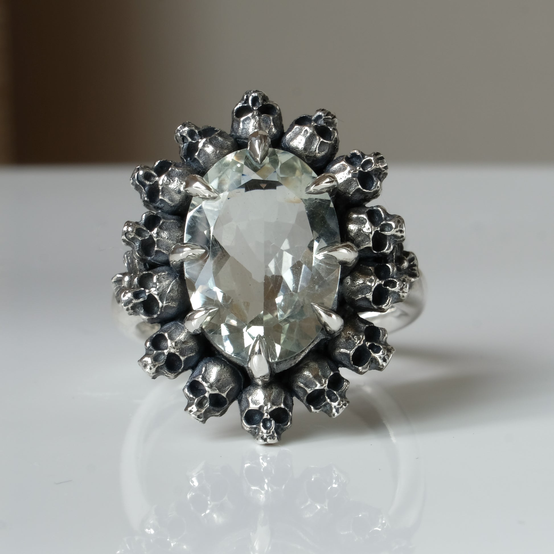 Ring with claw set with mint quartz gemstone and silver skull design on a white background