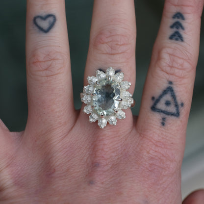 Ring with claw set mint quartz gemstone and silver skull design worn on tattooed had with neutral background