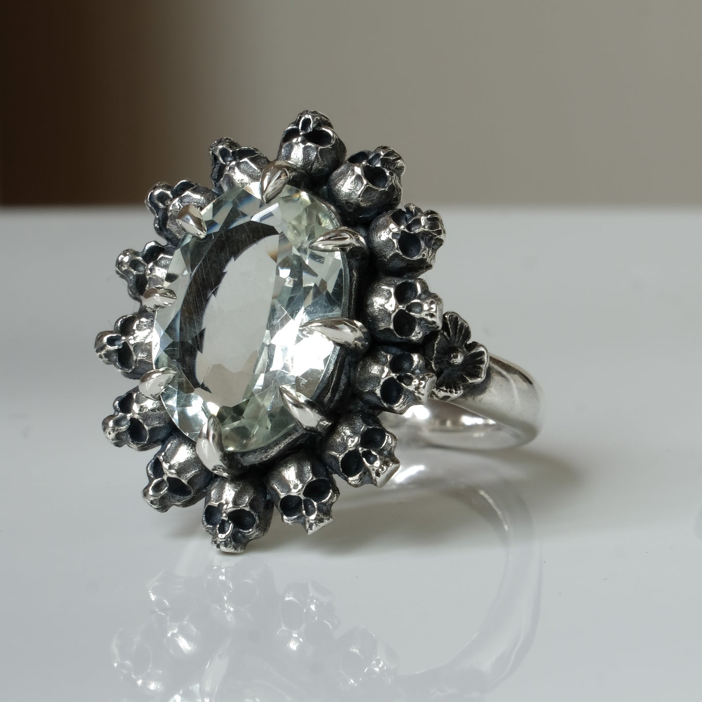Ring with claw set with mint quartz gemstone and silver skull design on a white background
