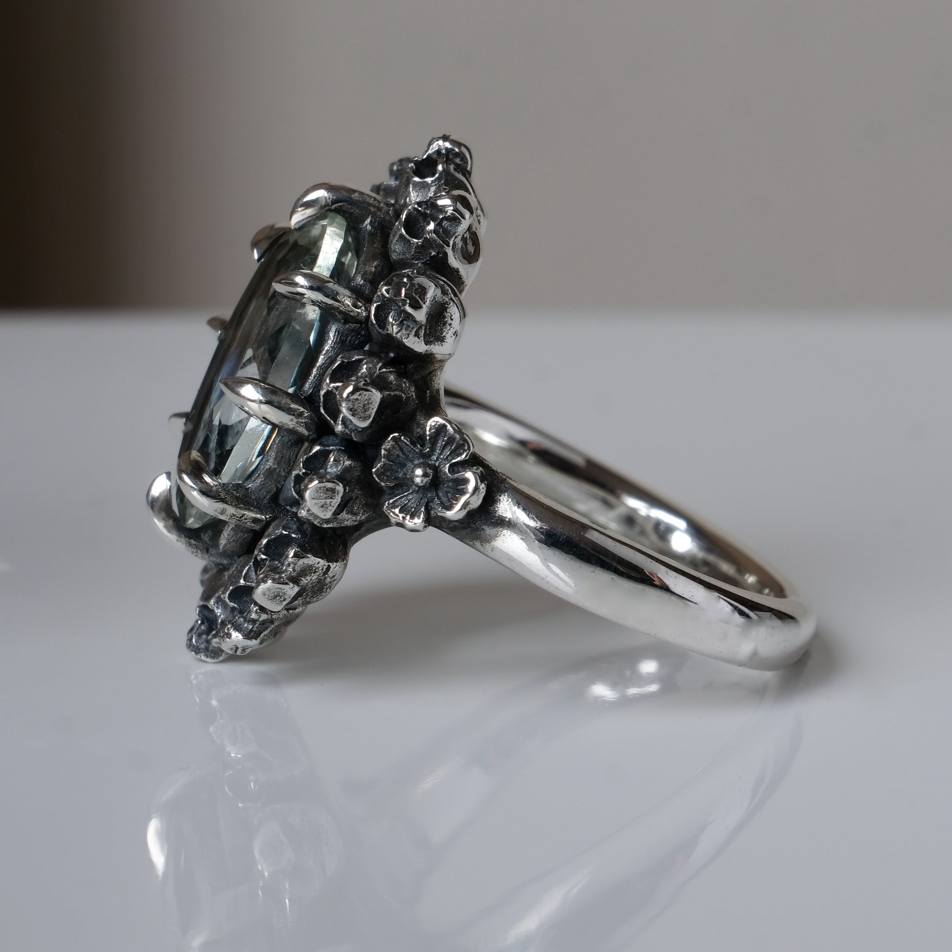 Ring with claw set with mint quartz gemstone and silver skull design on a white background