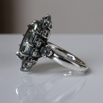Ring with claw set with mint quartz gemstone and silver skull design on a white background