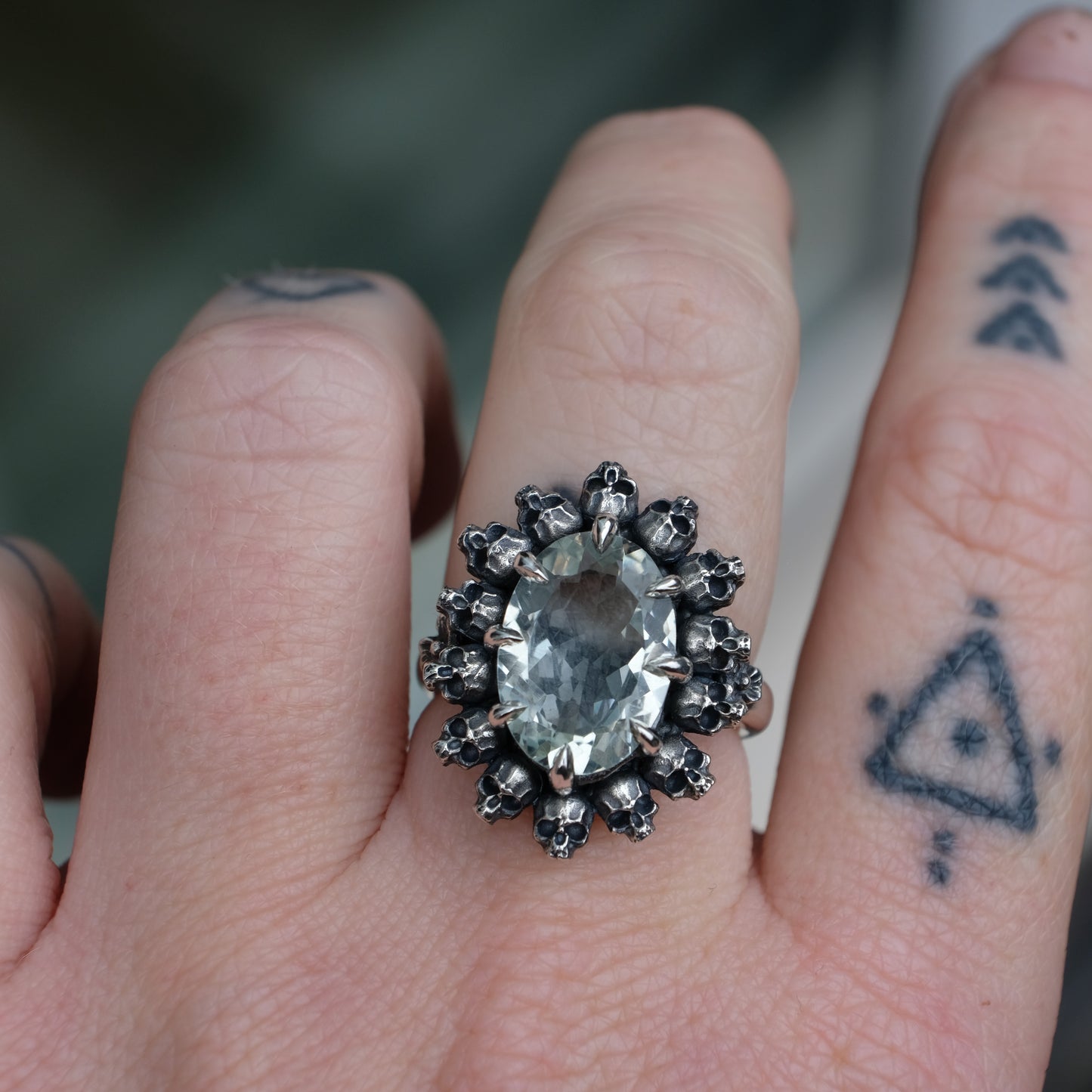 Ring with claw set with mint quartz gemstone and silver skull design worn on hand with tattooed fingers