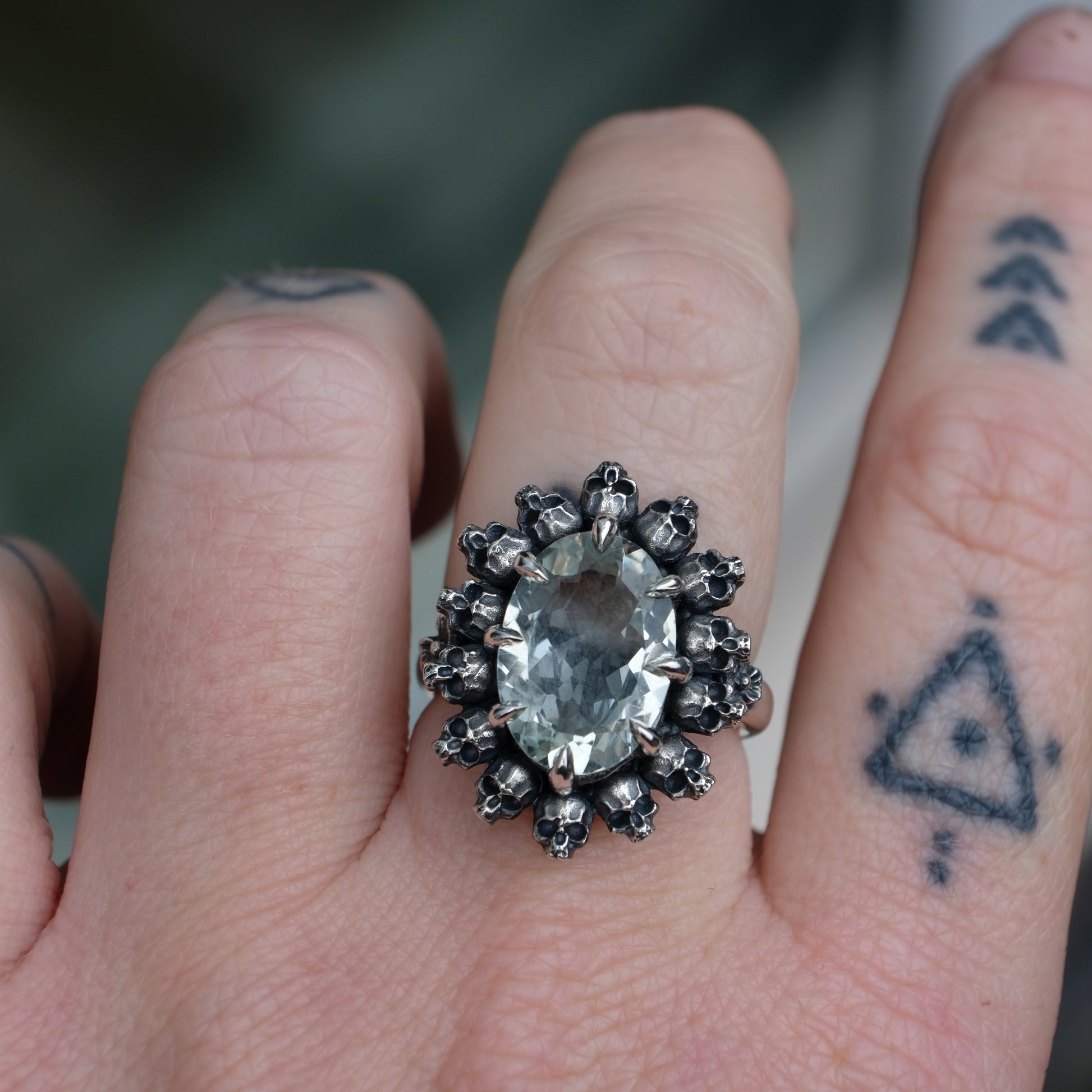 Ring with claw set with mint quartz gemstone and silver skull design worn on hand with tattooed fingers