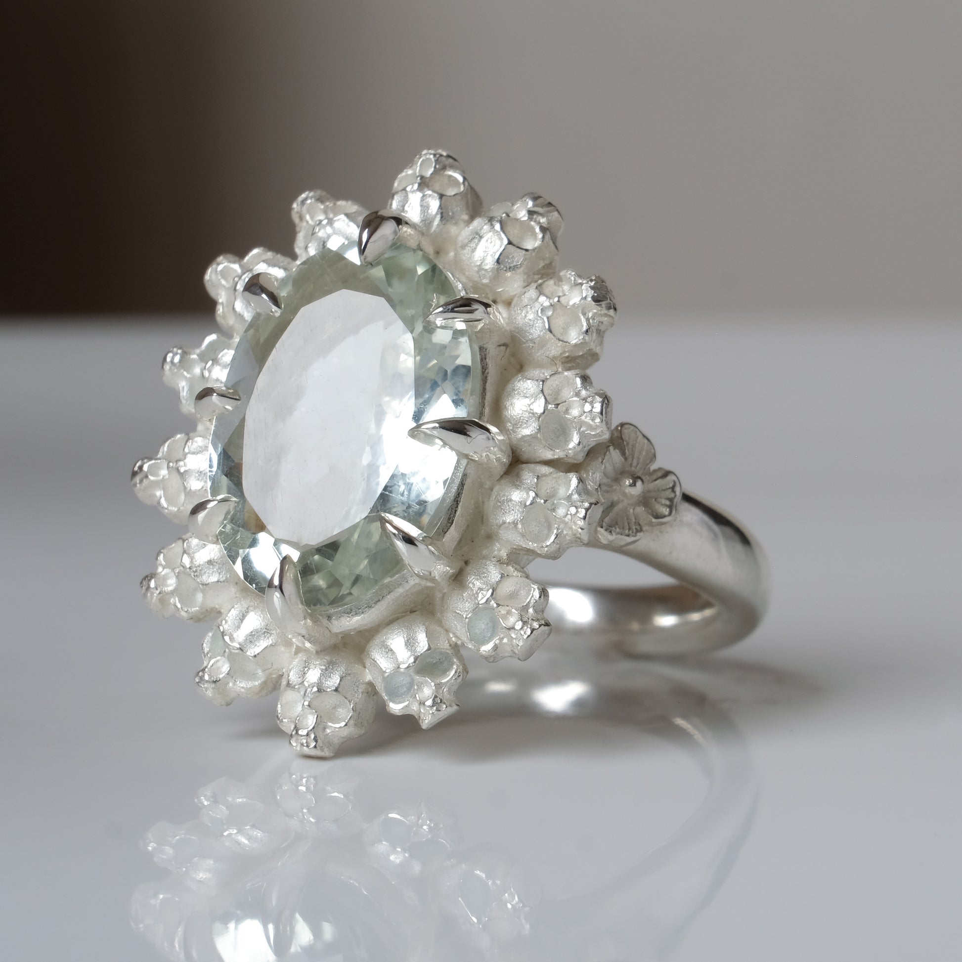 Ring with claw set mint quartz gemstone and silver skull design on a white background
