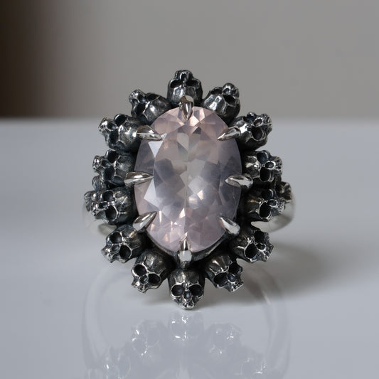 Ring claw set with rose quartz gemstone and silver skull halo design on a white background