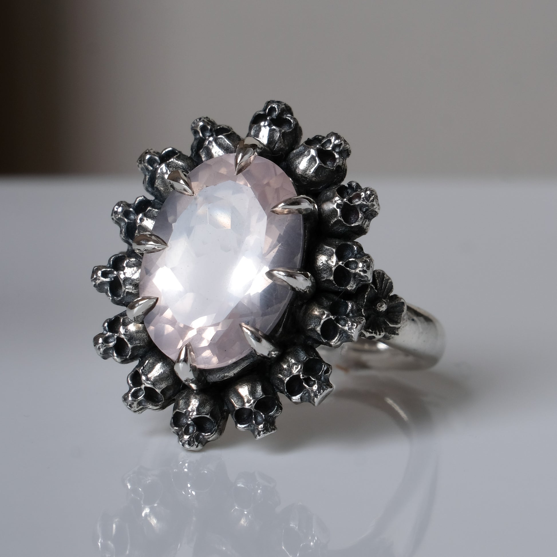 Ring claw set with rose quartz gemstone and silver skull halo design on a white background