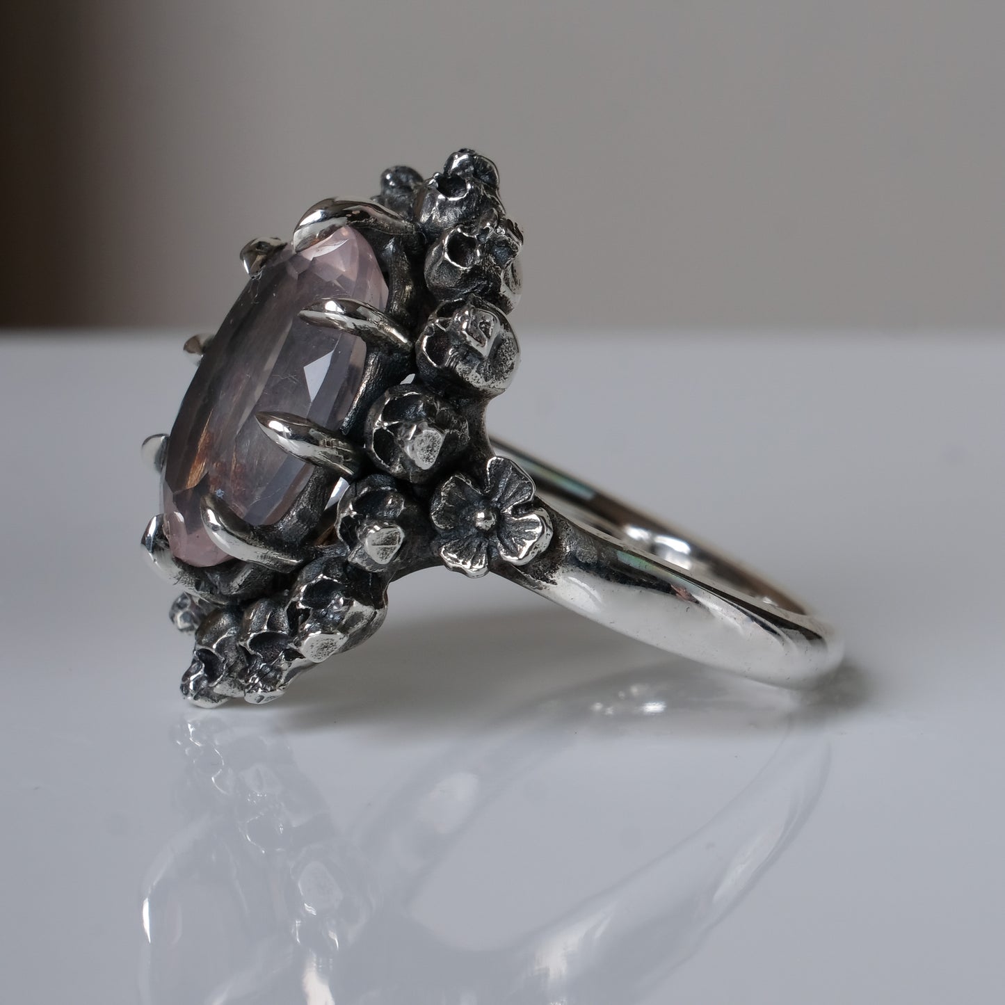 Ring claw set with rose quartz gemstone and silver skull halo design on a white background