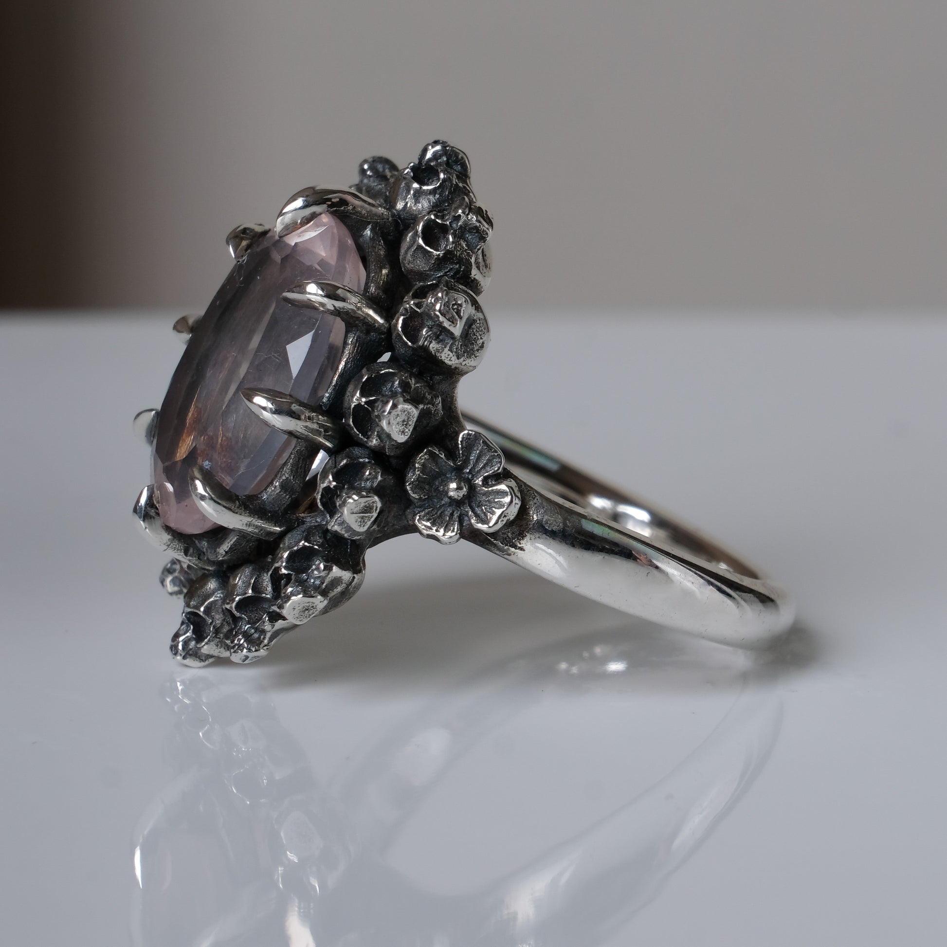 Ring claw set with rose quartz gemstone and silver skull halo design on a white background