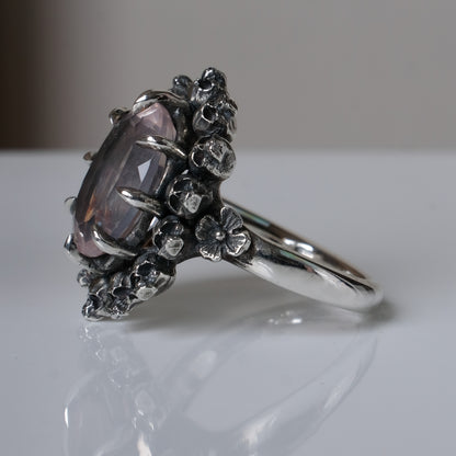 Ring claw set with rose quartz gemstone and silver skull halo design on a white background