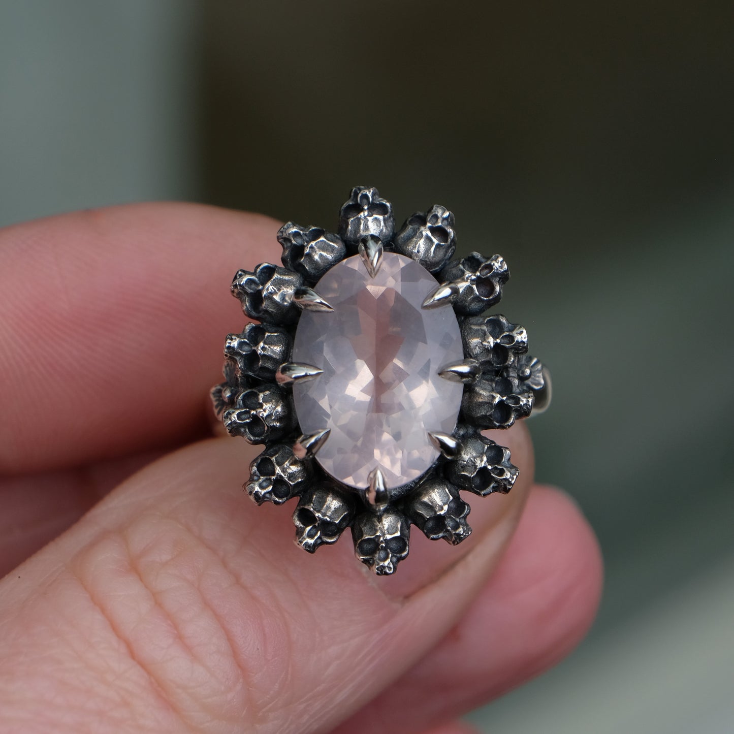 Ring claw set with rose quartz gemstone and silver skull halo design on a neutral background