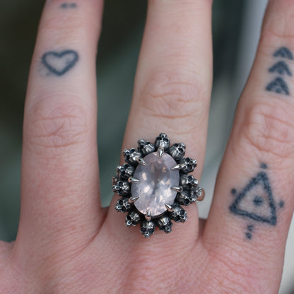 Ring claw set with rose quartz gemstone and silver skull halo design worn on hand with tattoos 