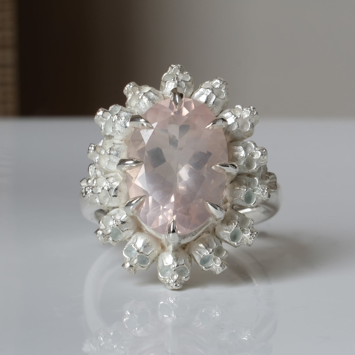 Ring claw set with rose quartz gemstone and silver skull halo design on a white background
