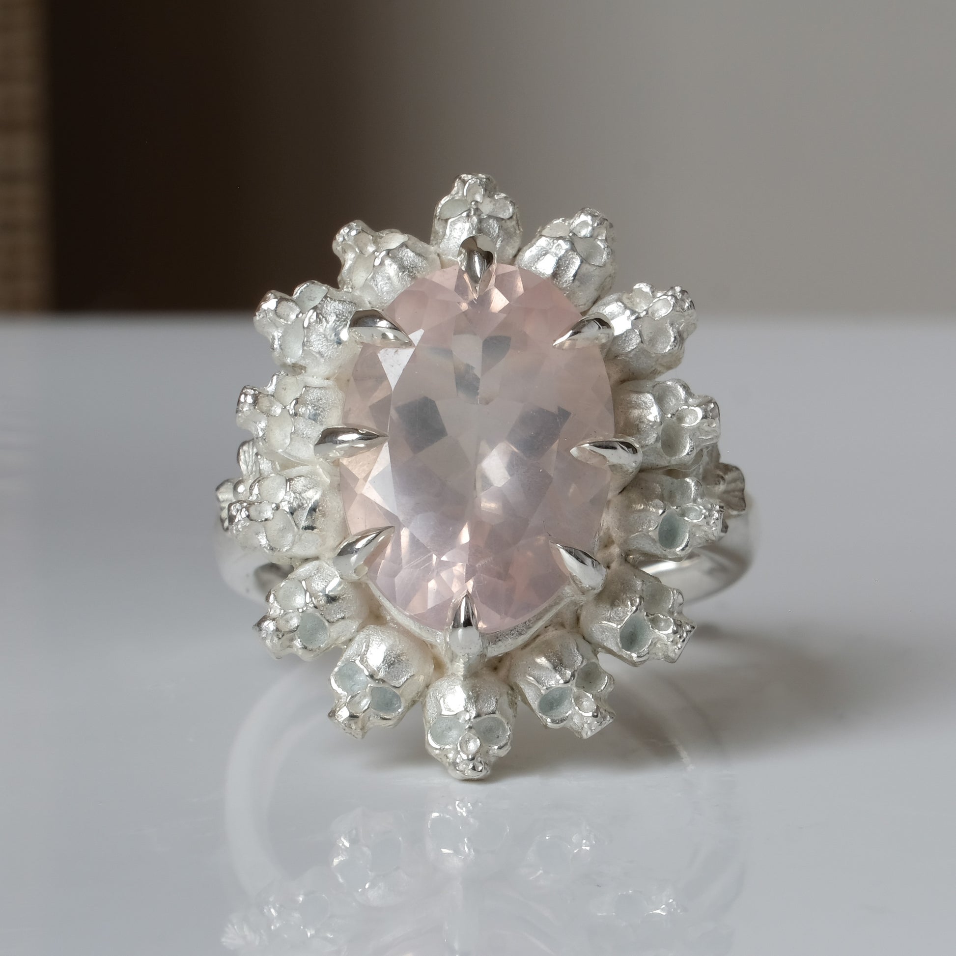 Ring claw set with rose quartz gemstone and silver skull halo design on a white background