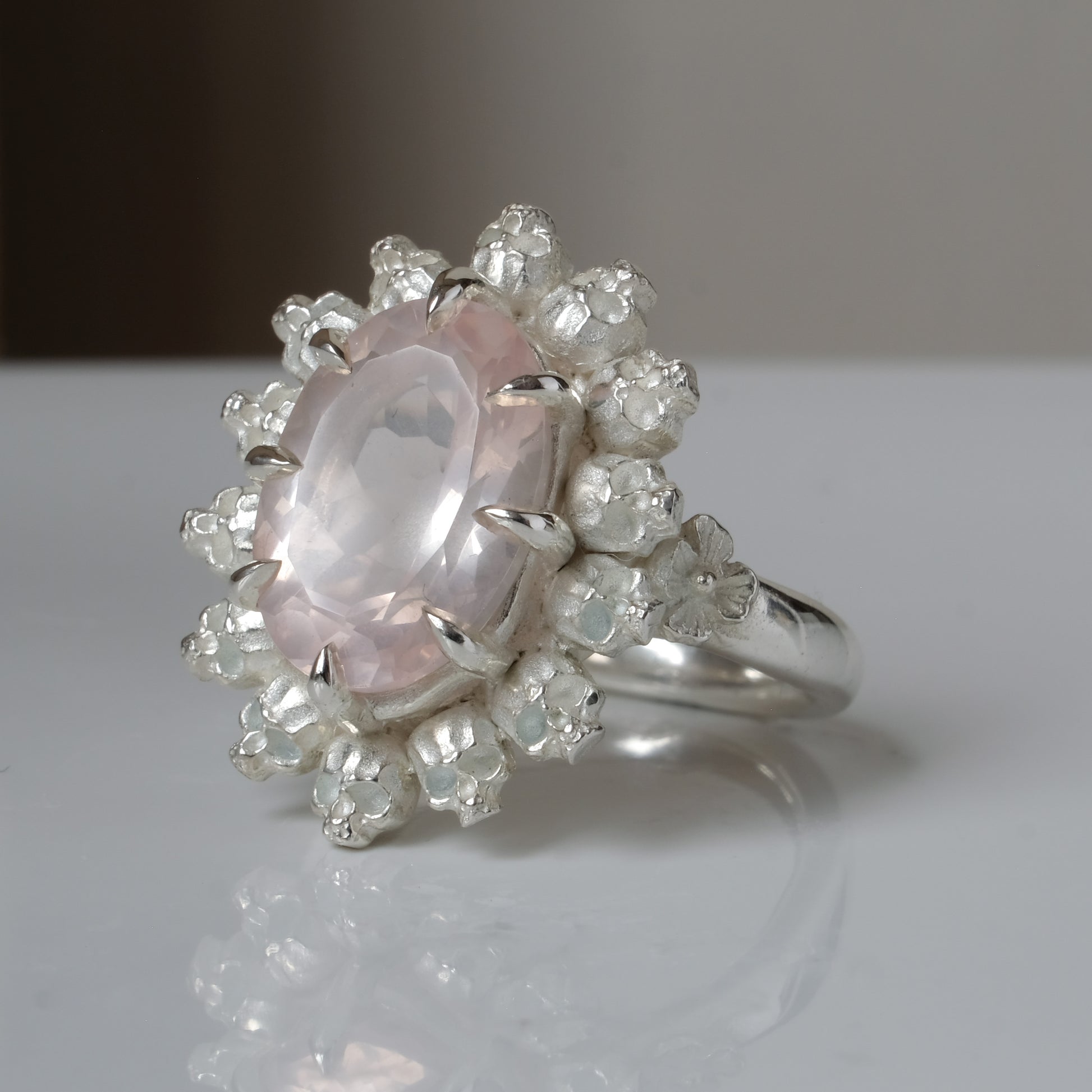 Ring claw set with rose quartz gemstone and silver skull halo design on a white background