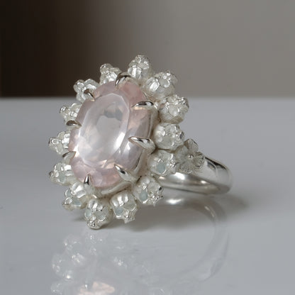Ring claw set with rose quartz gemstone and silver skull halo design on a white background
