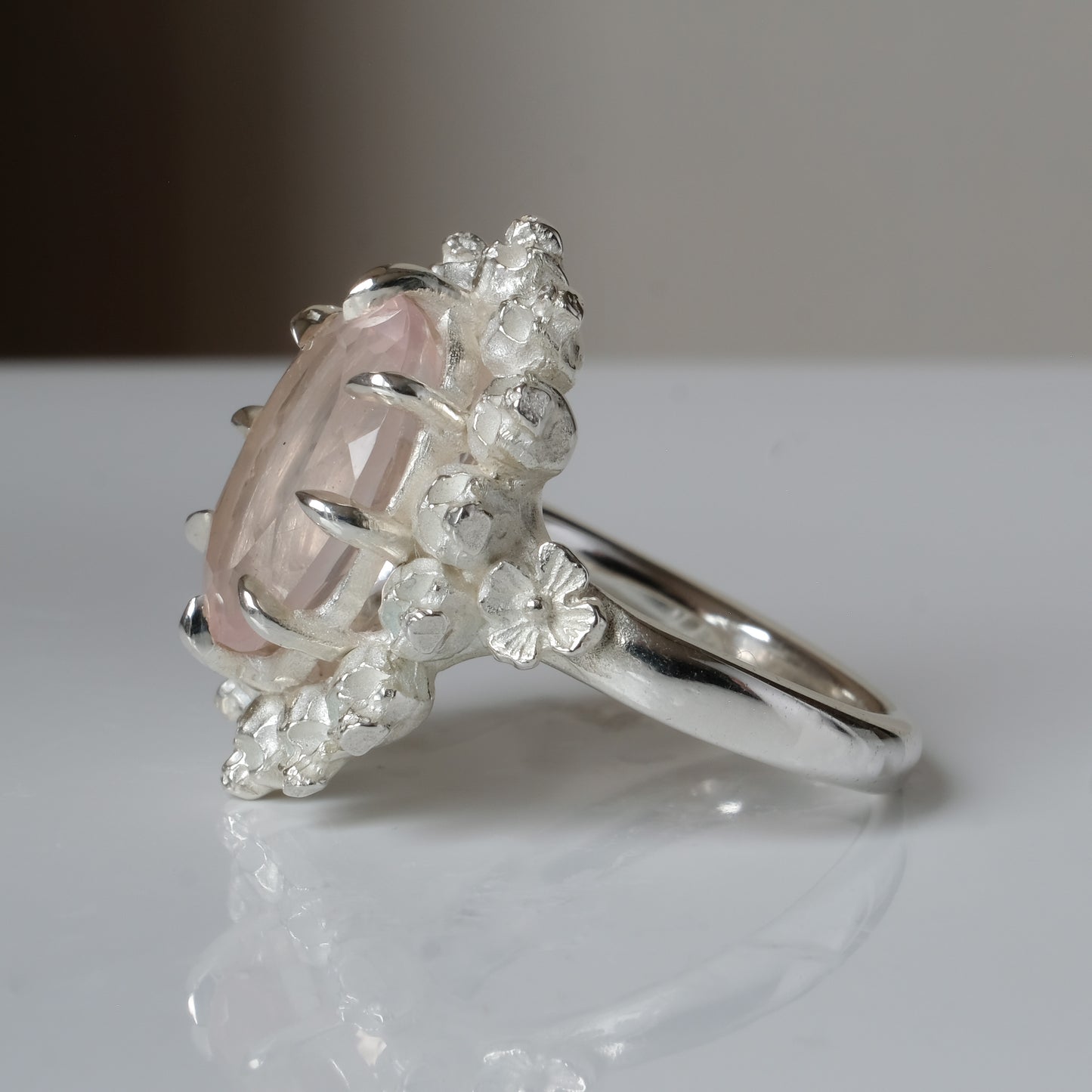 Ring claw set with rose quartz gemstone and silver skull halo design on a white background