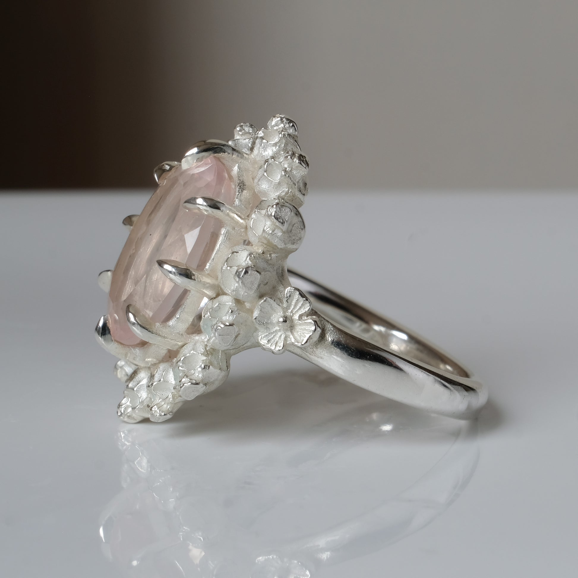Ring claw set with rose quartz gemstone and silver skull halo design on a white background