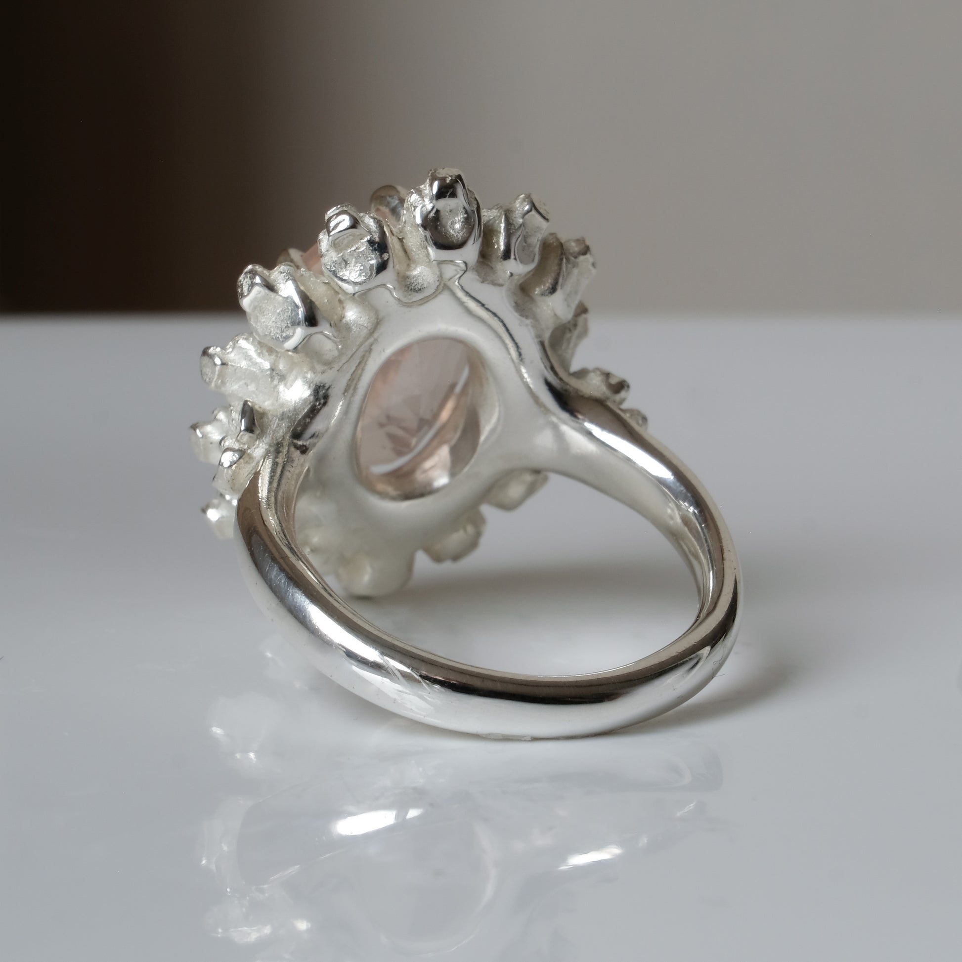 Ring claw set with rose quartz gemstone and silver skull halo design on a white background