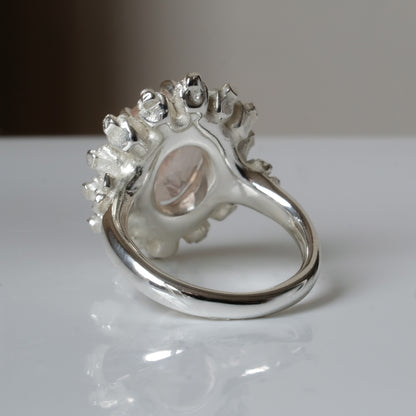 Ring claw set with rose quartz gemstone and silver skull halo design on a white background