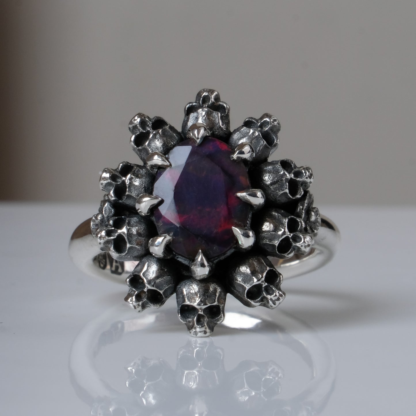 Silver ring with black opal gemstone in skull halo design on reflective background handmade in London, UK