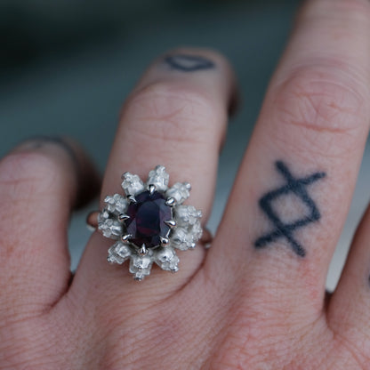 Silver ring with black opal gemstone in skull halo design worn on hand with tattoos handmade in London, UK