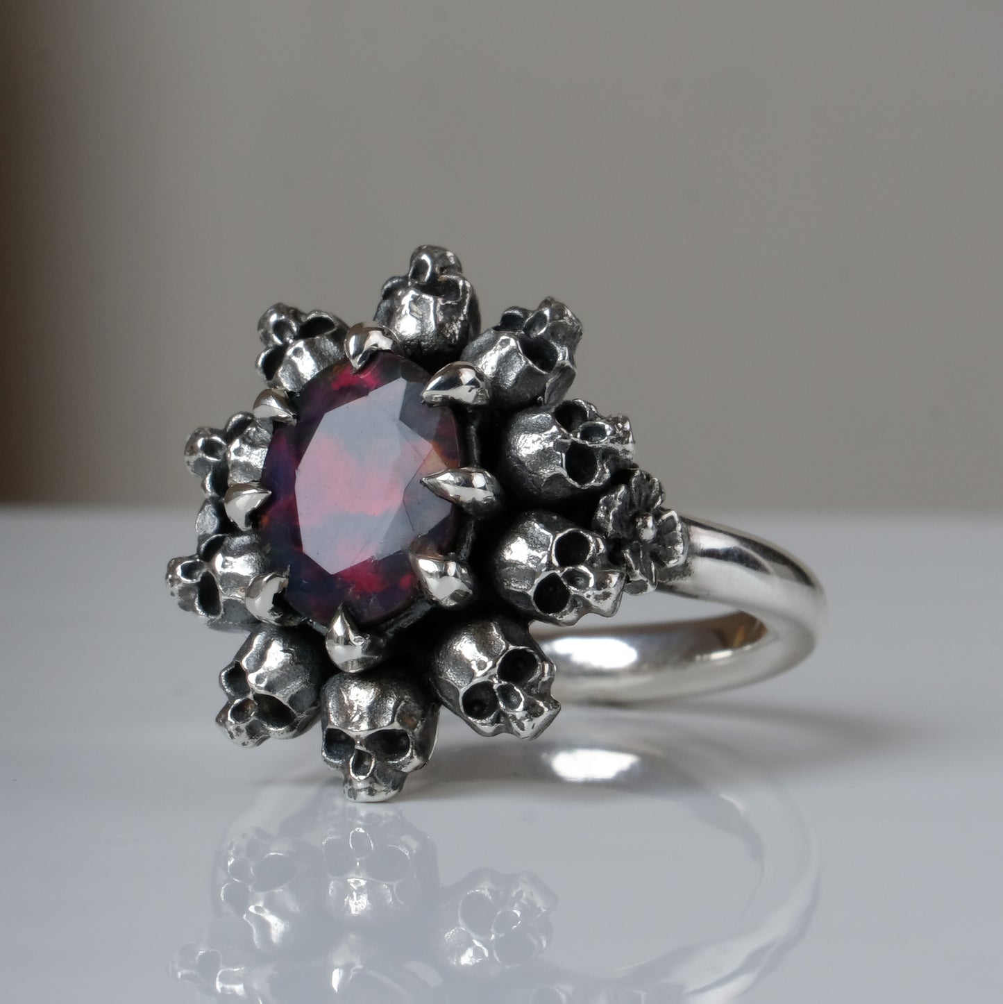 Silver ring with black opal gemstone in skull halo design on reflective background handmade in London, UK