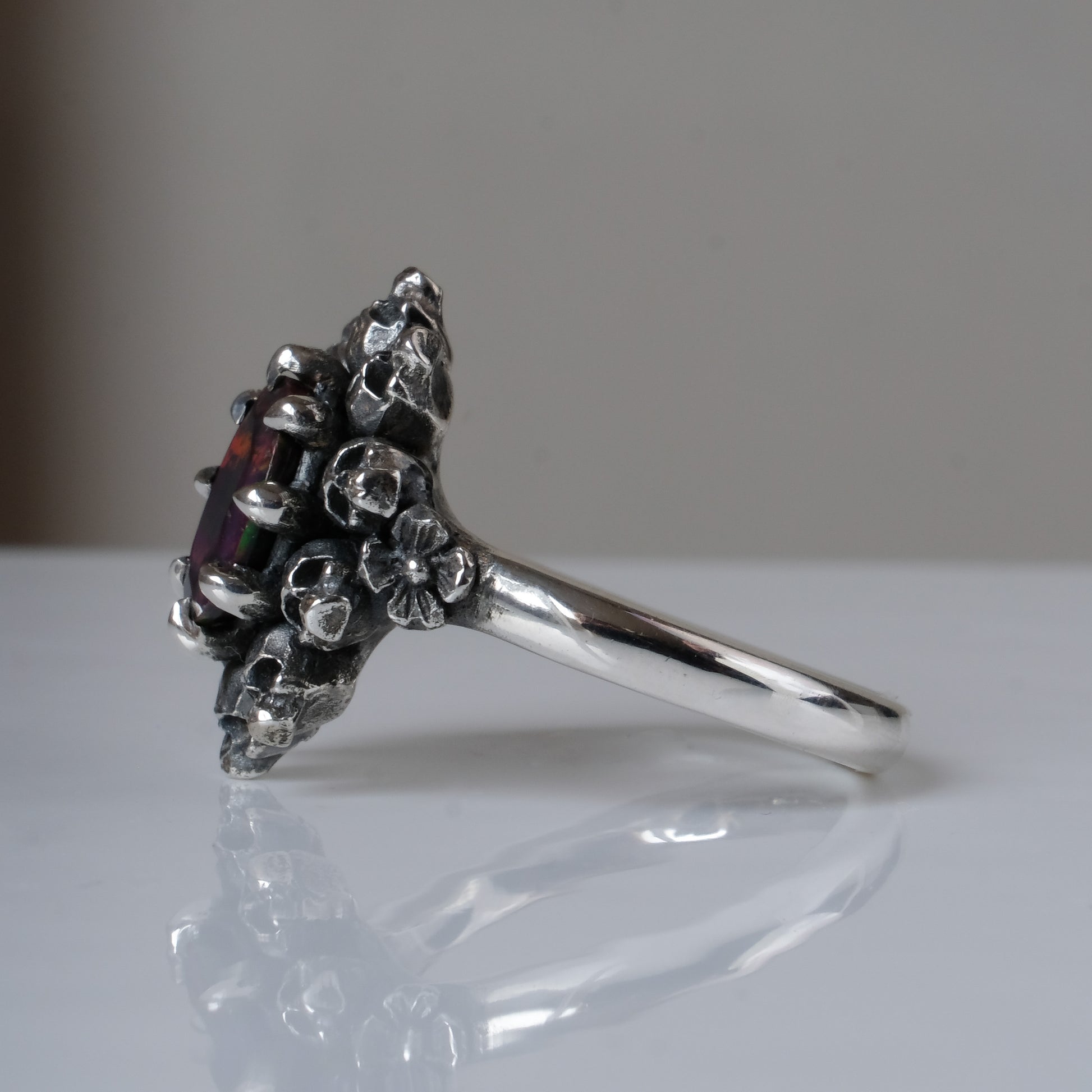 Silver ring with black opal gemstone in skull halo design on reflective background handmade in London, UK