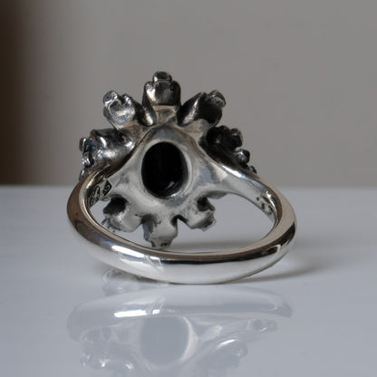 Silver ring with black opal gemstone in skull halo design on reflective background handmade in London, UK