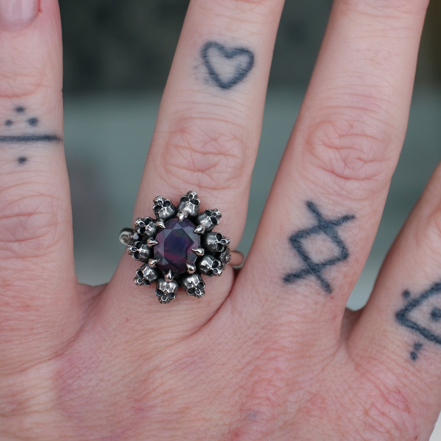 Silver ring with black opal gemstone in skull halo design worn on hand with tattoos handmade in London, UK