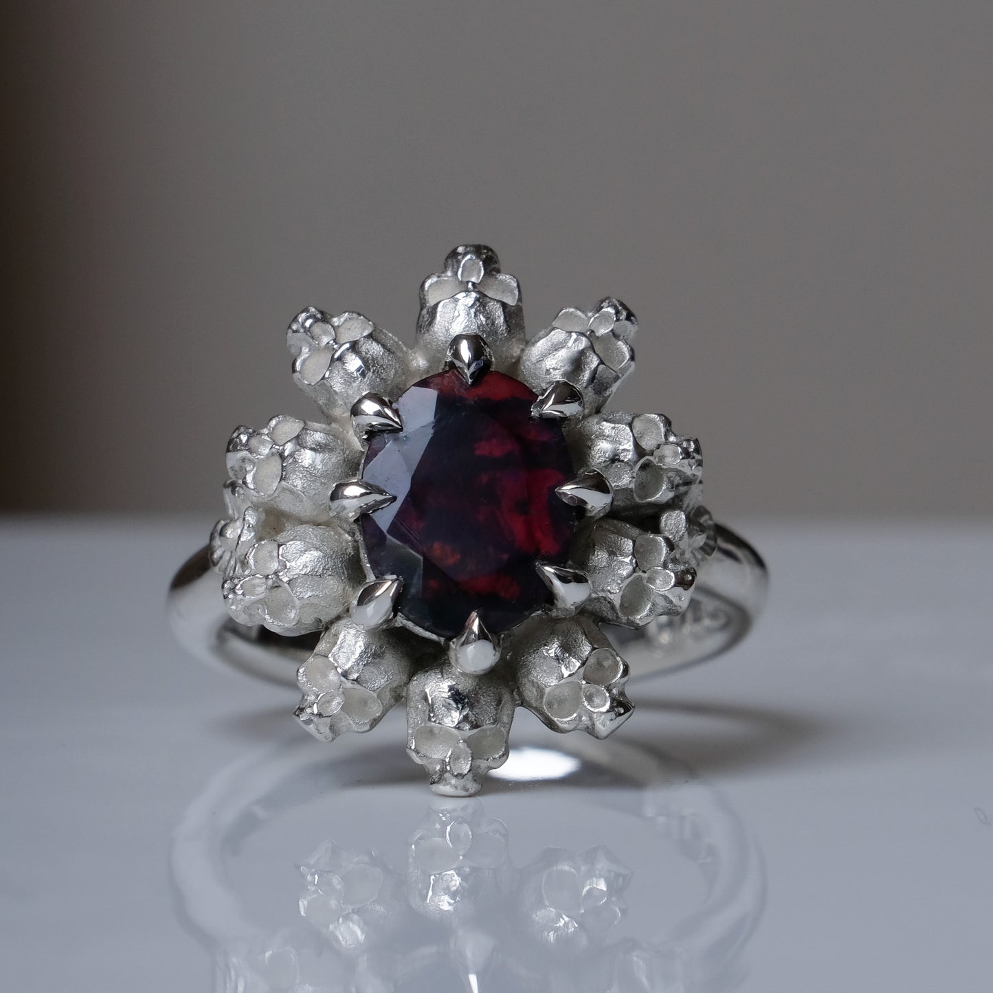 Silver ring with black opal gemstone in skull halo design on reflective background handmade in London, UK