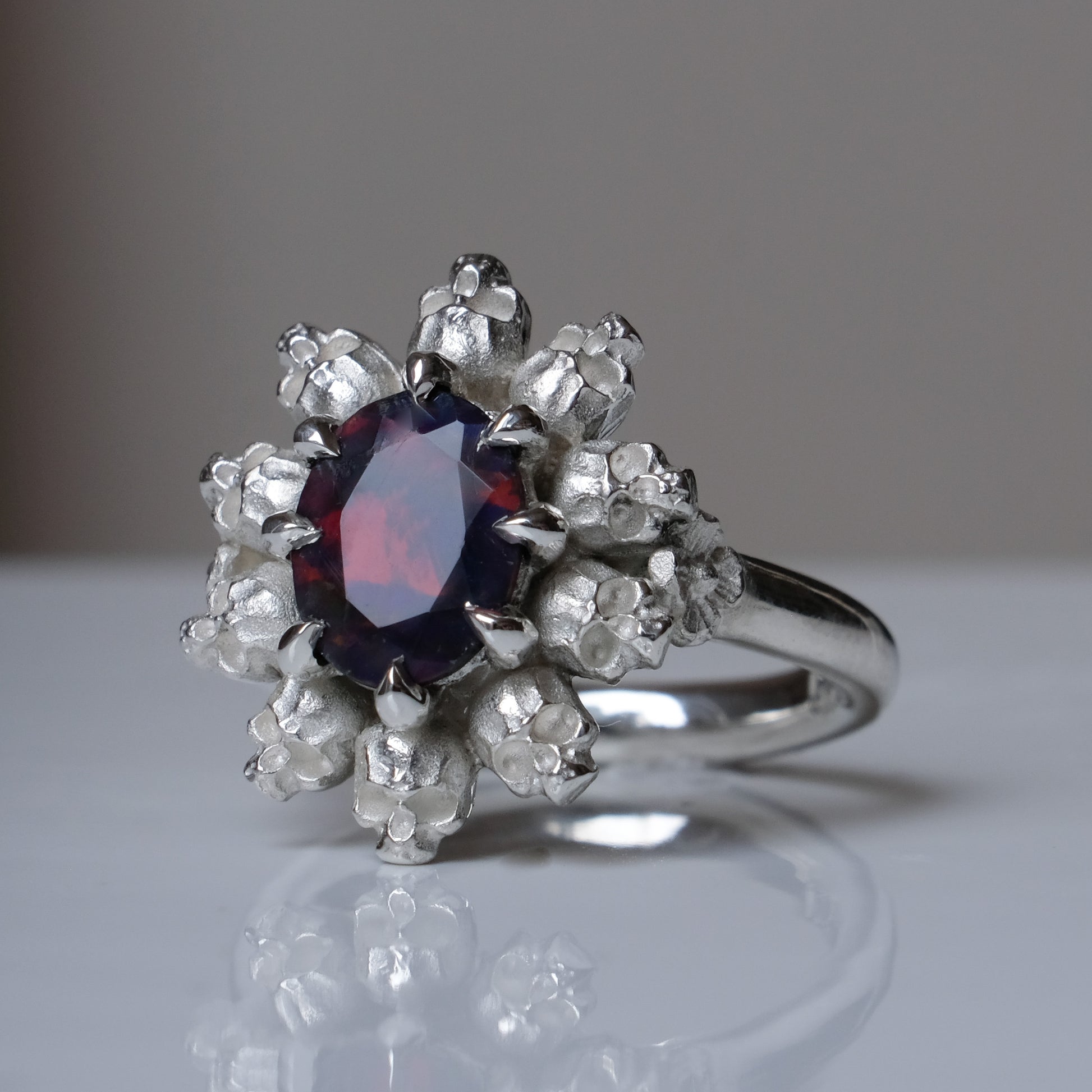 Silver ring with black opal gemstone in skull halo design on reflective background handmade in London, UK