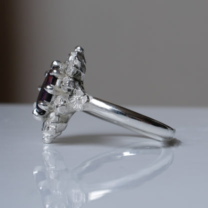 Silver ring with black opal gemstone in skull halo design on reflective background handmade in London, UK