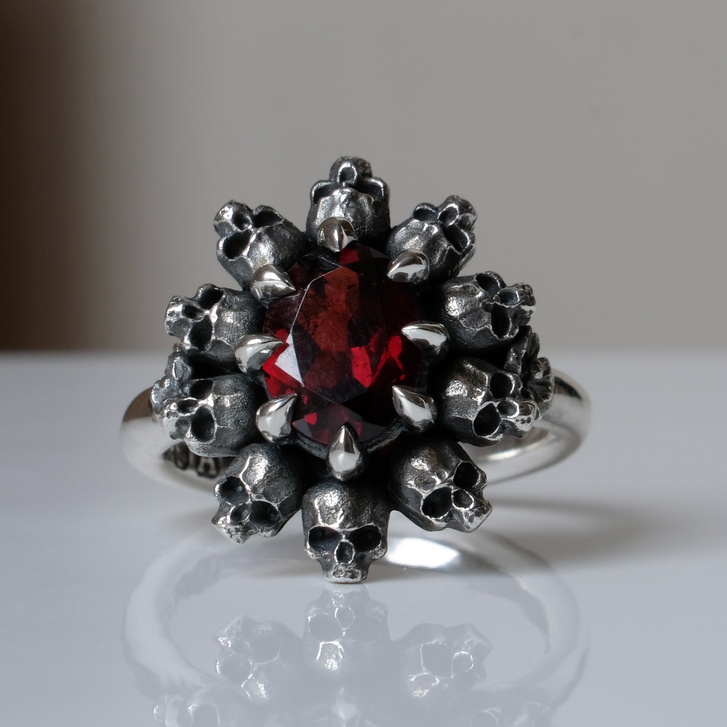 Silver ring with red garnet stone in skull halo design on reflective background 