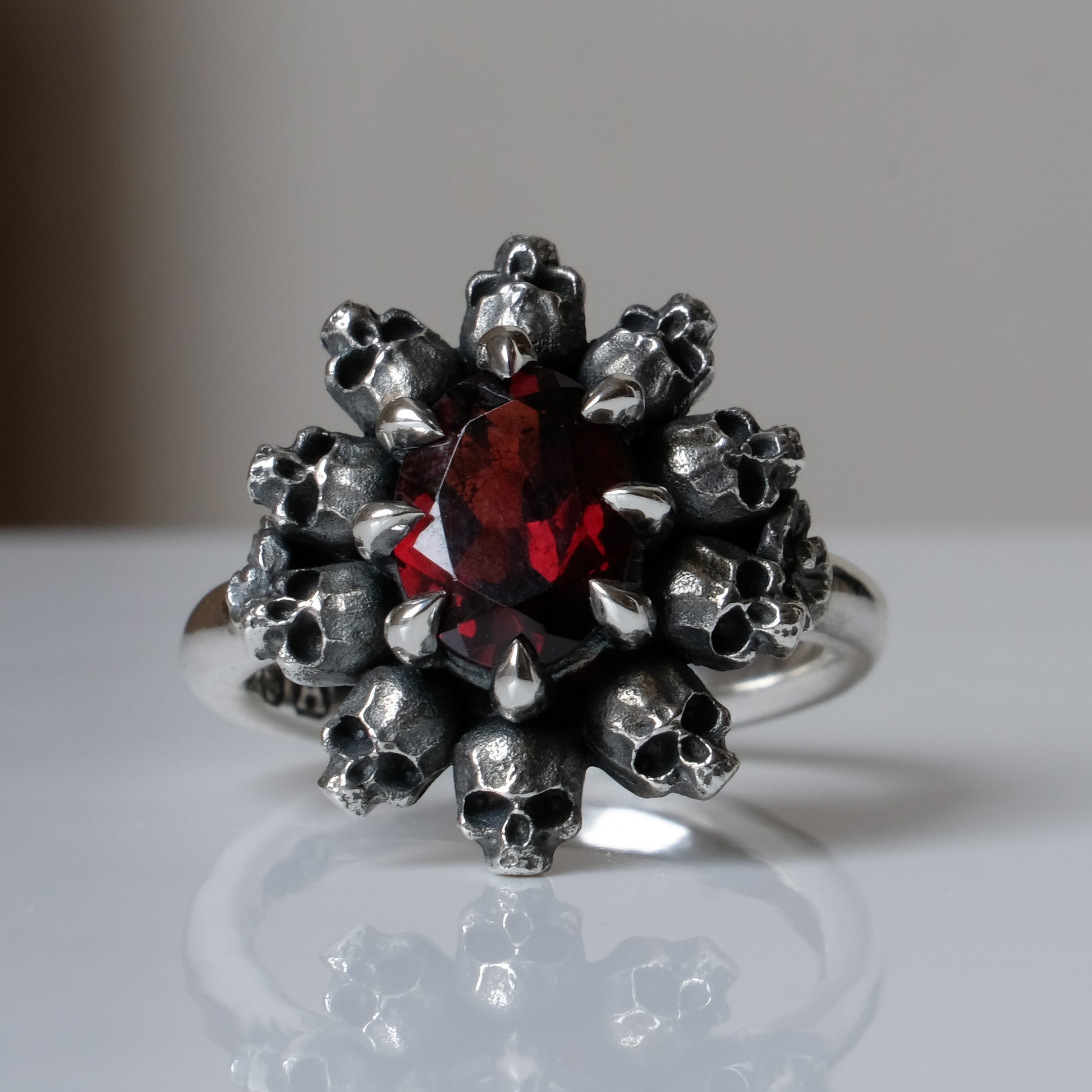 Silver ring with red garnet stone in skull halo design on reflective background 