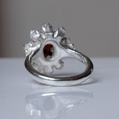 Silver ring with red garnet stone in skull halo design on reflective background handmade in London, UK
