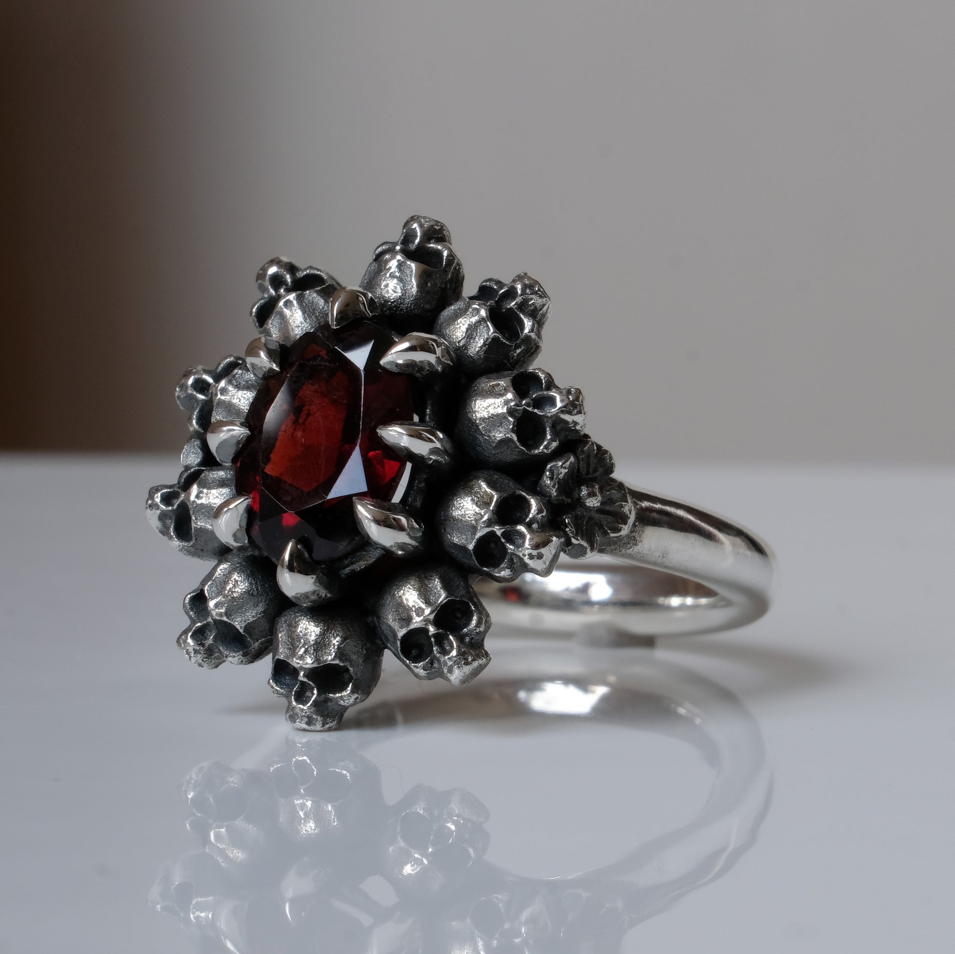 Silver ring with red garnet stone in skull halo design on reflective background handmade in London, UK