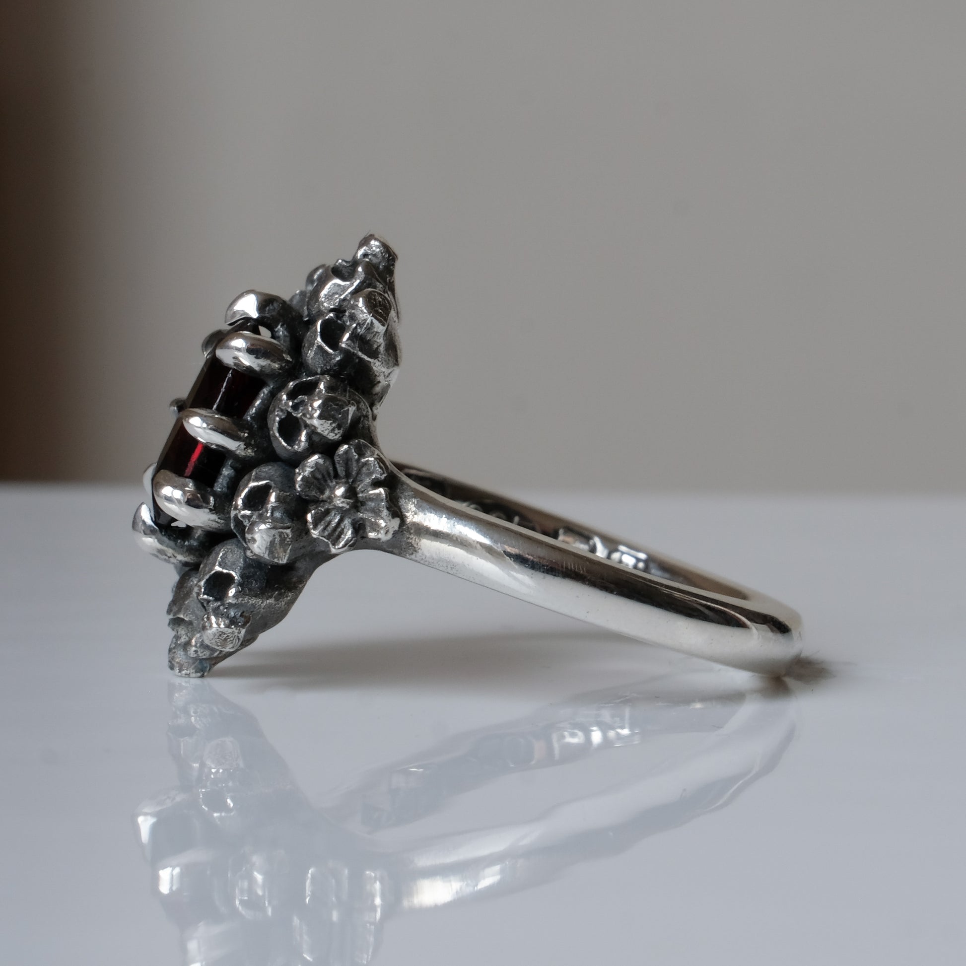 Silver ring with red garnet stone in skull halo design on reflective background handmade in London, UK