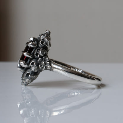 Silver ring with red garnet stone in skull halo design on reflective background handmade in London, UK