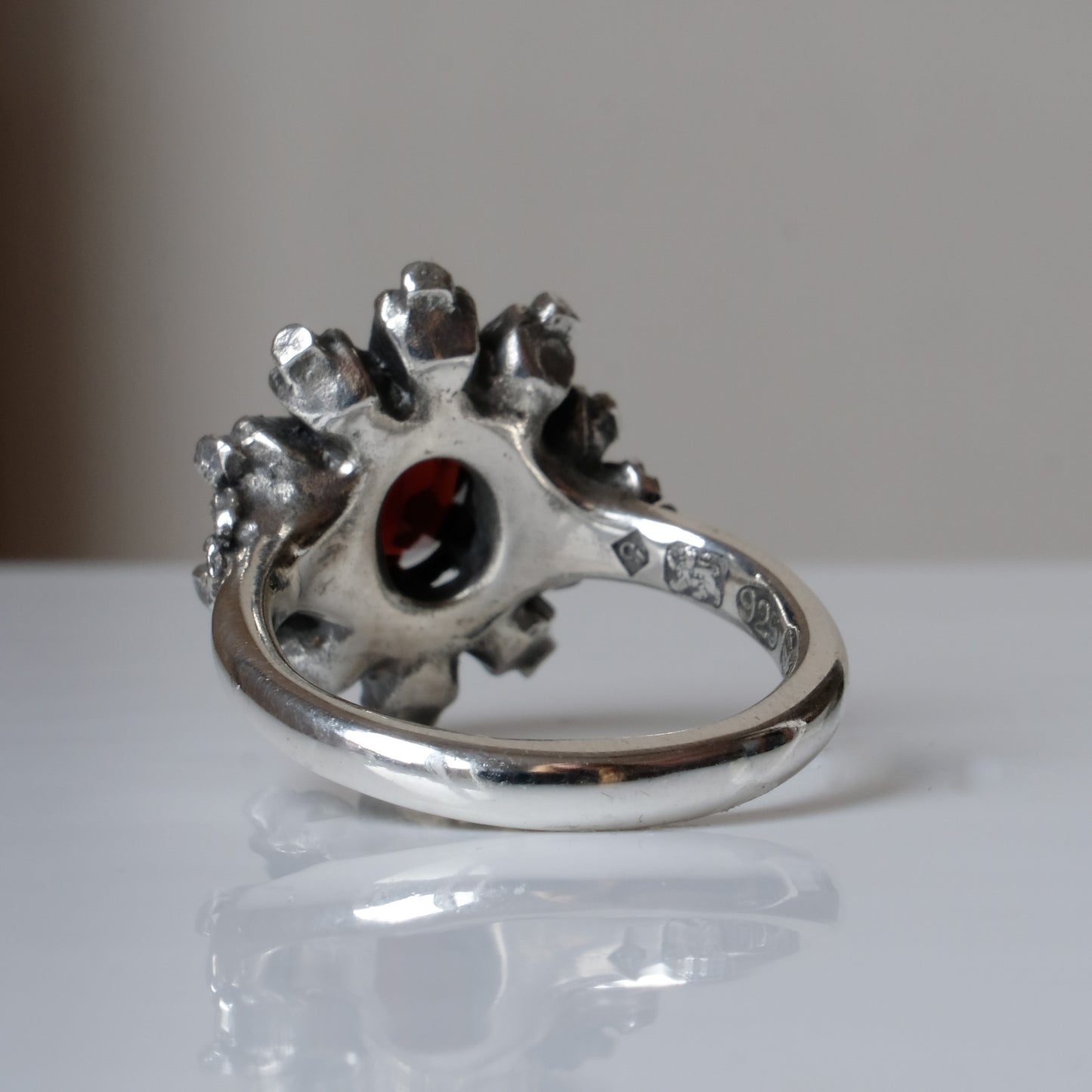 Silver ring with red garnet stone in skull halo design on reflective background handmade in London, UK