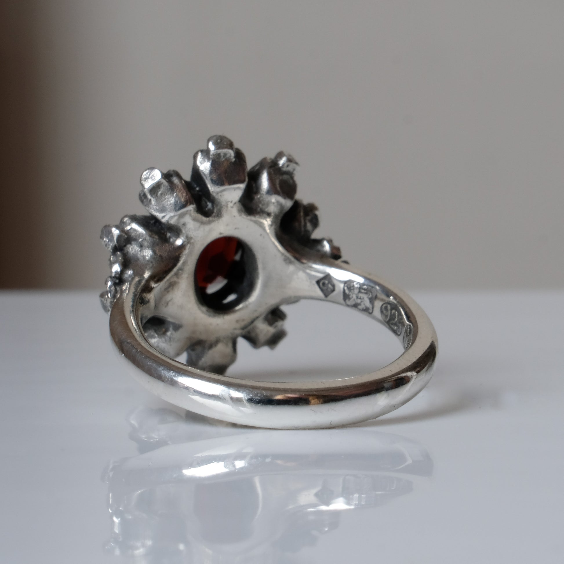 Silver ring with red garnet stone in skull halo design on reflective background handmade in London, UK
