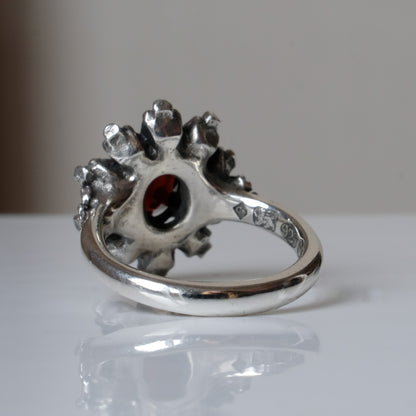 Silver ring with red garnet stone in skull halo design on reflective background handmade in London, UK