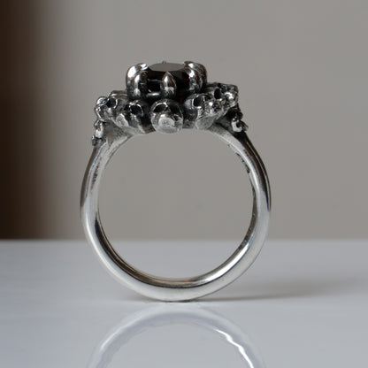 Silver ring with red garnet stone in skull halo design on reflective background handmade in London, UK