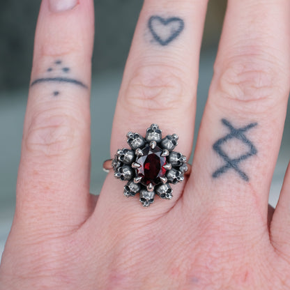 Silver ring with red garnet stone in skull halo design on worn on hand with tattoos handmade in London, UK