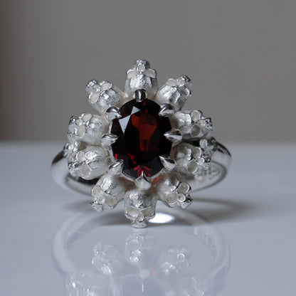 Silver ring with red garnet stone in skull halo design on reflective background handmade in London, UK