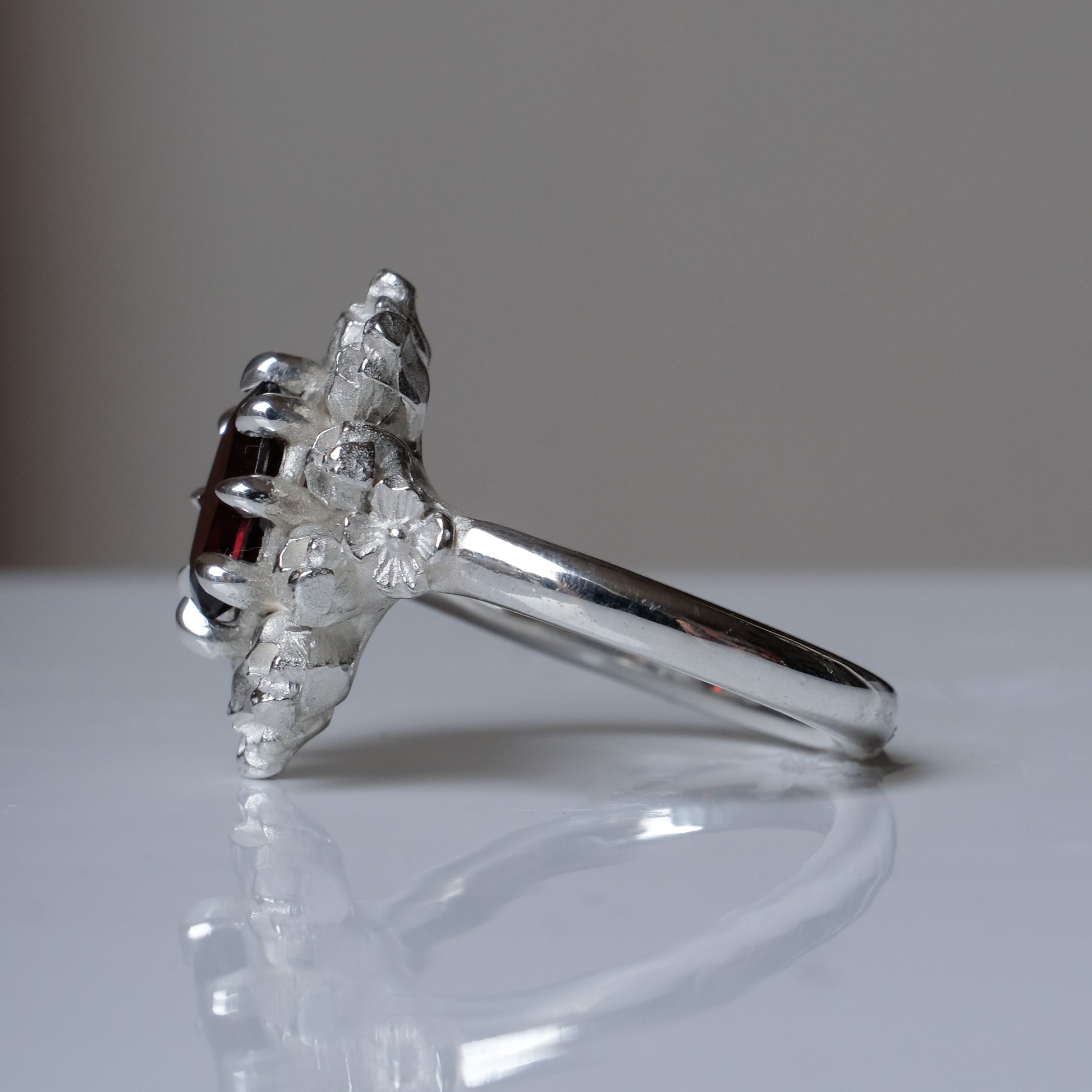 Silver ring with red garnet stone in skull halo design on reflective background handmade in London, UK