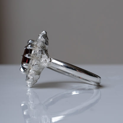 Silver ring with red garnet stone in skull halo design on reflective background handmade in London, UK