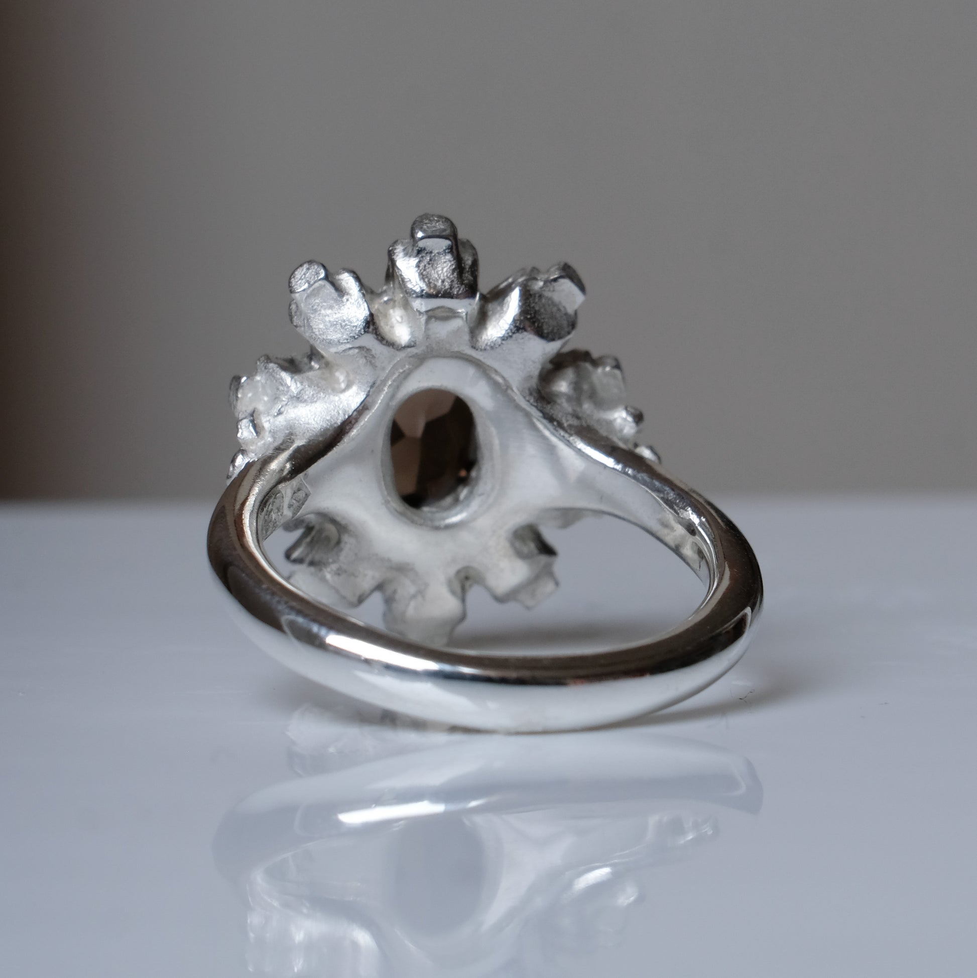 Silver ring with brown smokey quartz gemstone in skull halo design on reflective background handmade in London, UK